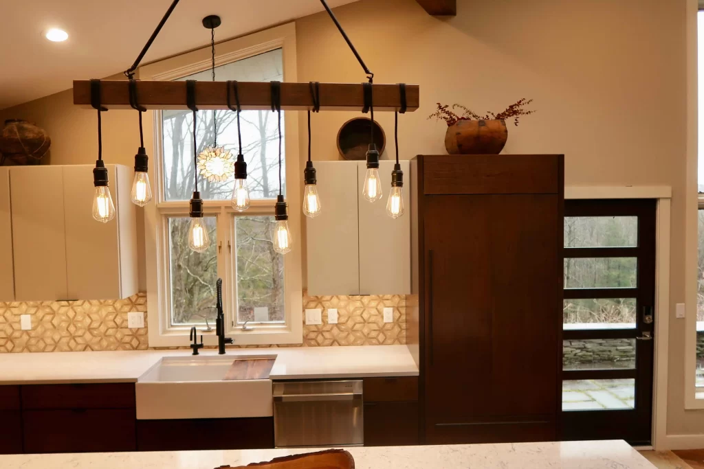 Rustic kitchen remodel by NEPA Builders featuring a farmhouse sink, warm wood cabinetry, unique pendant lighting, and a scenic view in Lake Ariel