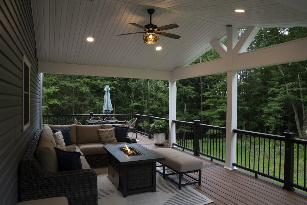 Spacious outdoor living space showing the seamless transition from the vaulted covered porch to the open deck area, overlooking a wooded backyard.