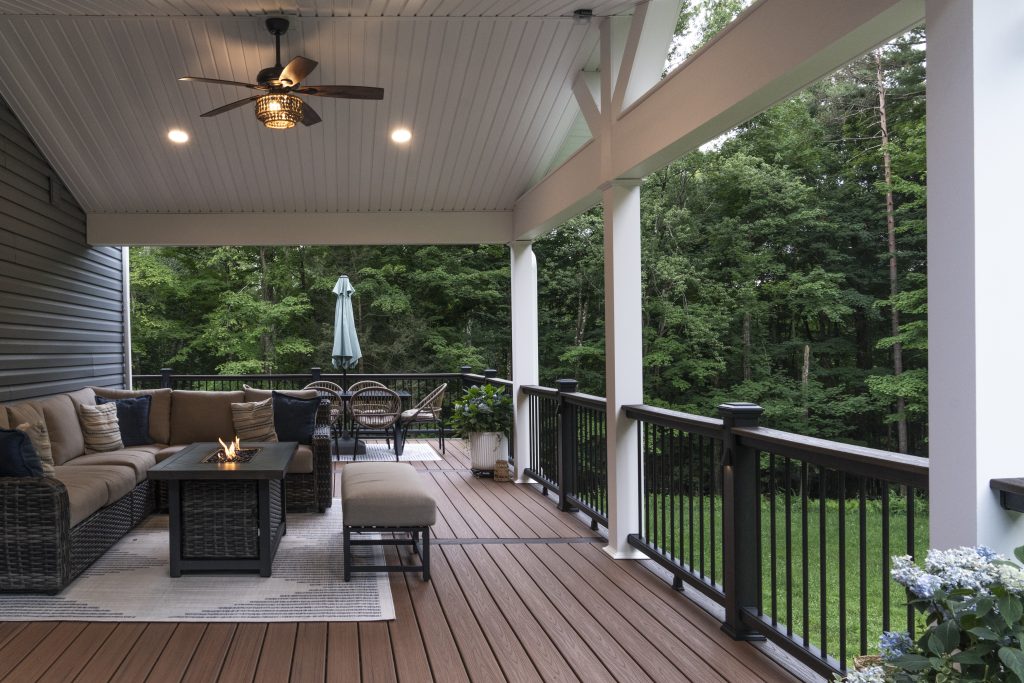 Open-air section of a new composite deck featuring a rectangular dining table with a sage green umbrella and wicker chairs, surrounded by black aluminum railings.